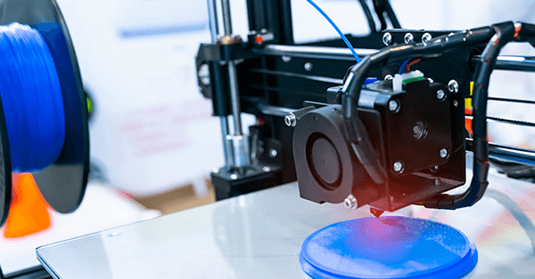 Ein 3D-Drucker erstellt ein rundes, blaues Objekt auf einer glatten Plattform.