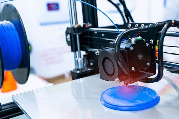 Ein 3D-Drucker erstellt ein rundes, blaues Objekt auf einer glatten Plattform.