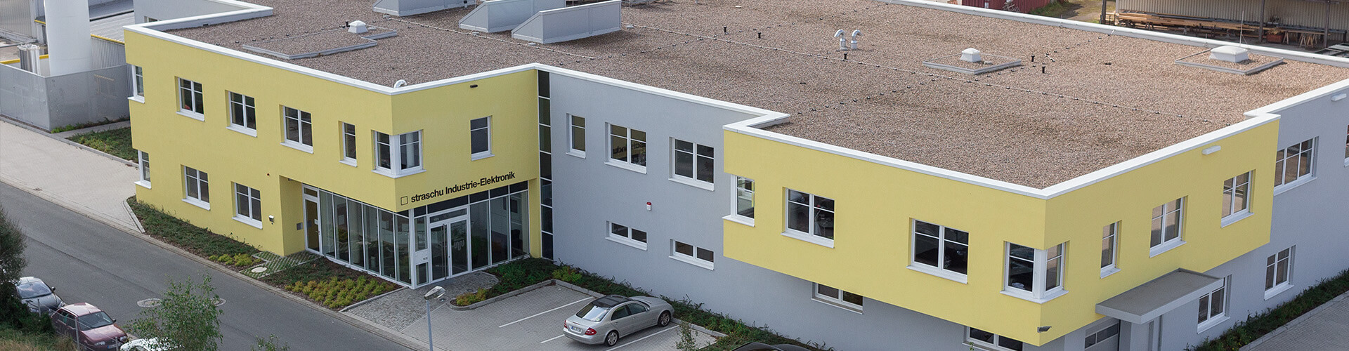 Das gelbe Gebäude der straschu Industrie-Elektrobnik GmbH aus der Flugansicht.